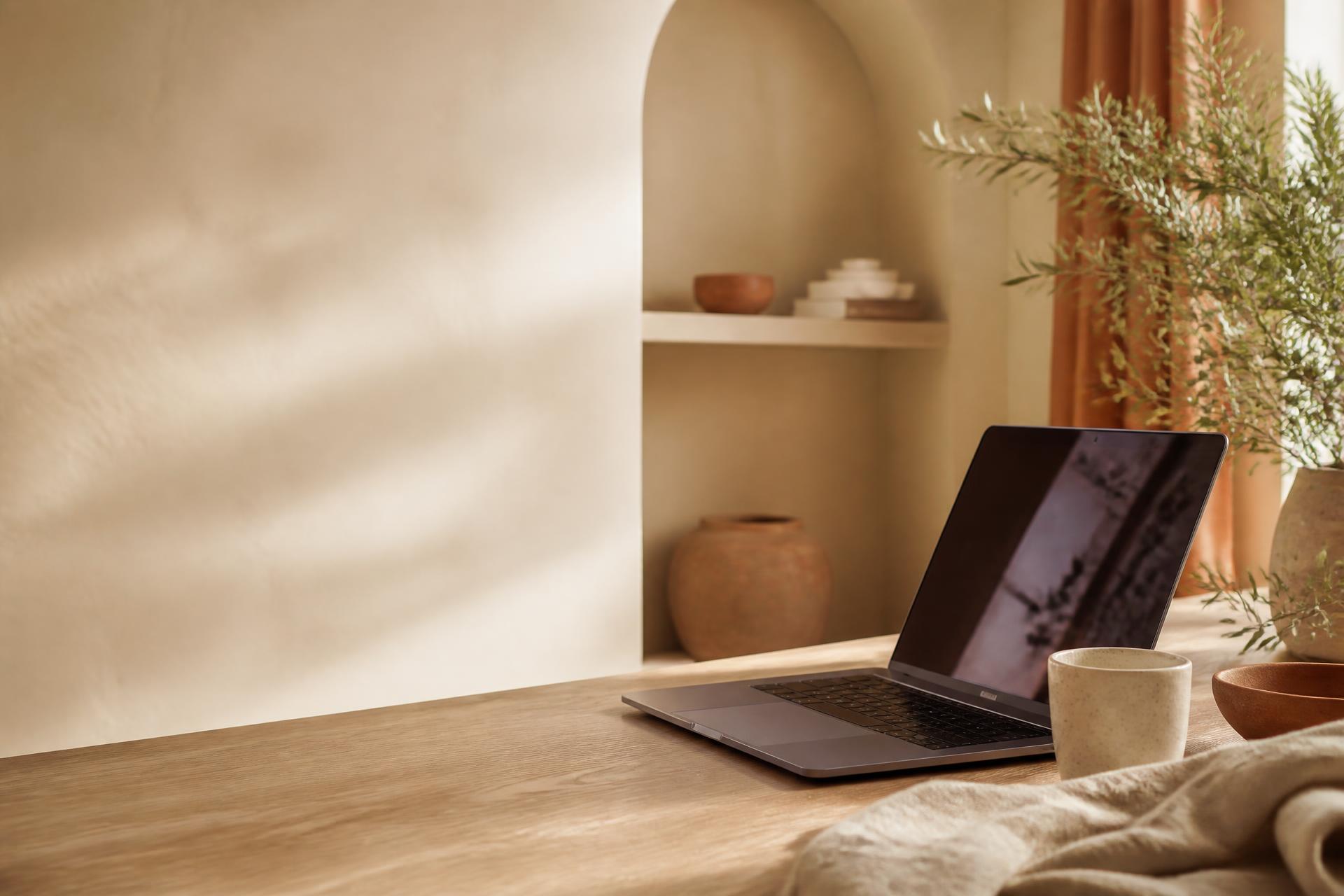 Warmes, lichtdurchflutetes Kreativstudio mit Laptop, Kaffeetasse und Pflanze